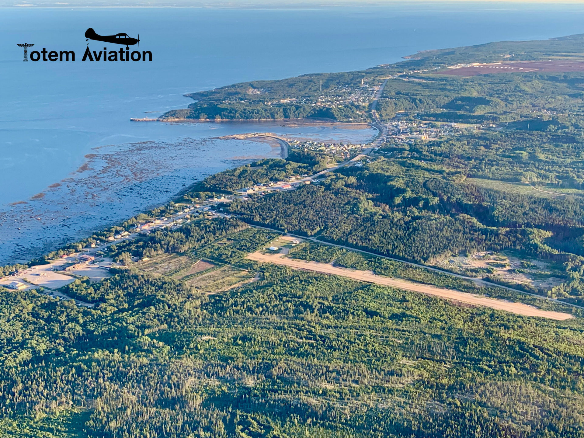 Vue aérienne des Escoumins : le village en bord de fleuve, la piste de l'aérodrome et le Saint-Laurent